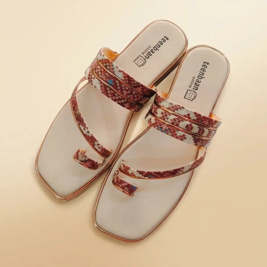 A pair of women's slide sandals with square toes, featuring a white footbed and straps decorated with a red, brown, and gold floral pattern, set against a solid beige background.